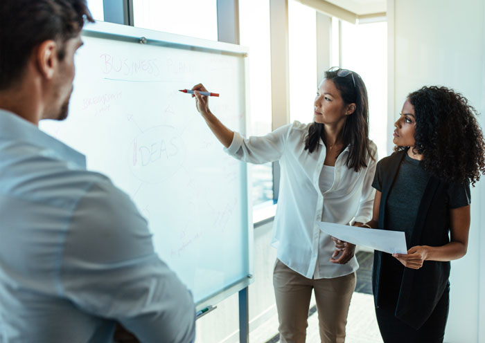 Group of young professions working at a white board calculating effects of group health insurance for their business